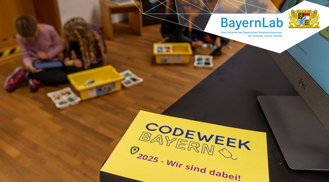 Foto mit Blick in einen Raum, im Hintergrund sind unscharf mehrere Kinder zu sehen, die am Boden sitzen und gerade an LEGO Robotern bauen, im Vordergrund ist ein gelber Zettel zu sehen auf dem 